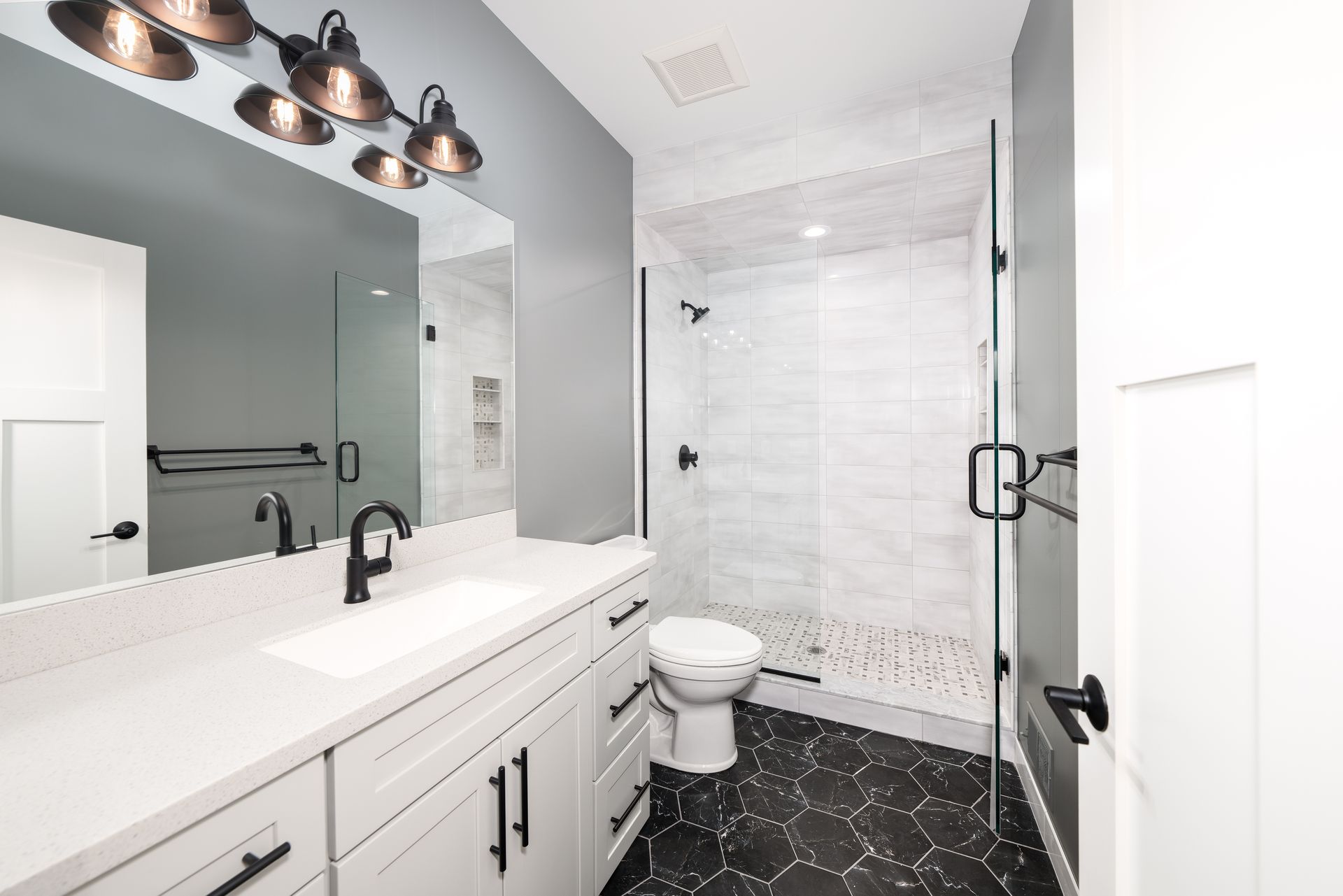 Modern bathroom with white vanity, large mirror, and black hexagon tile floor
