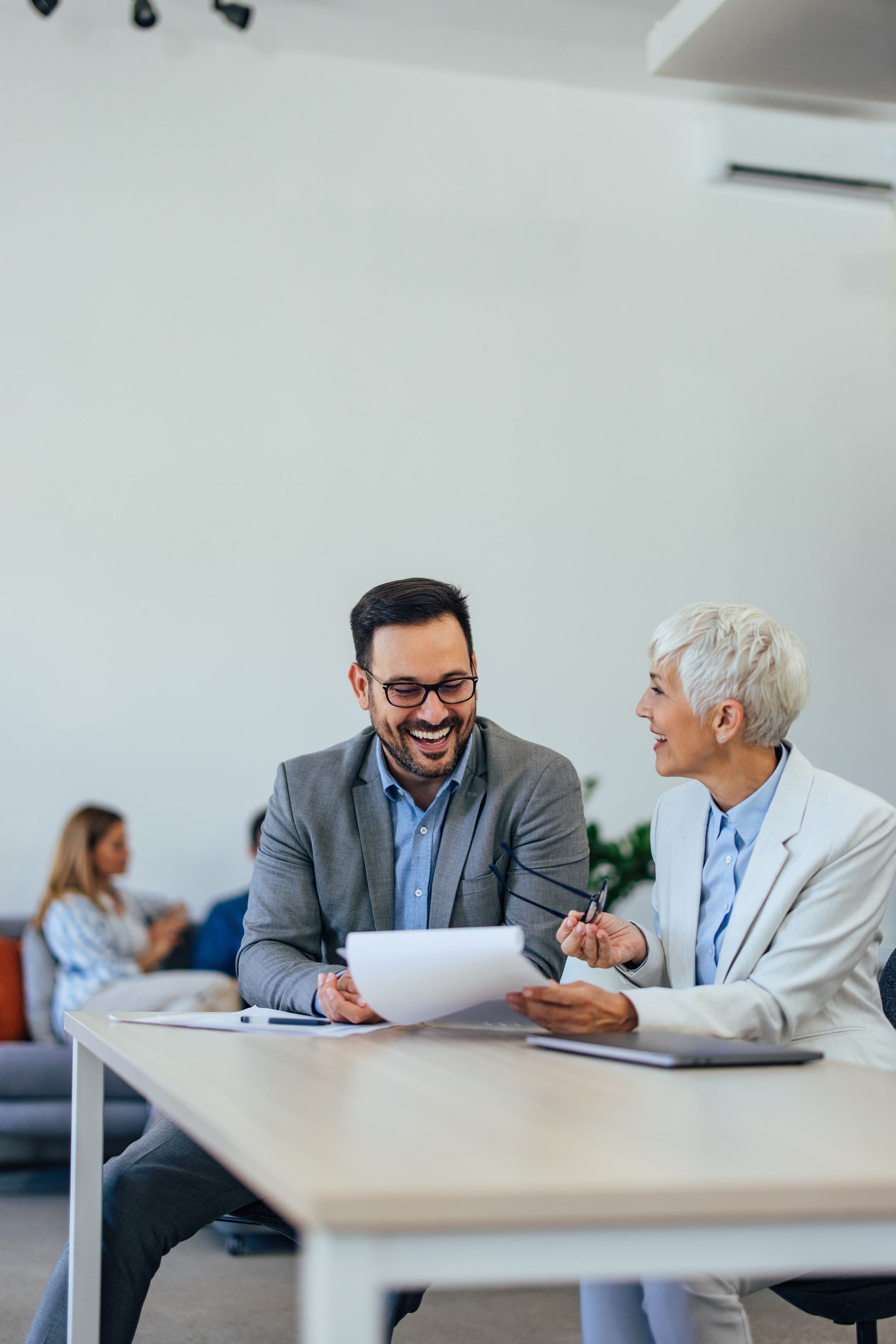 Two coworkers smiling and talking over papers at a conference table in a bright office