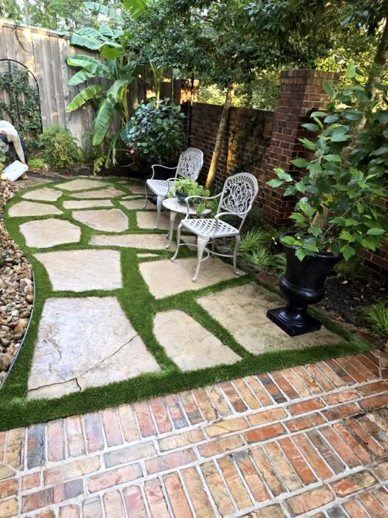 Patio with flagstones and artificial turf, seating area, brick border, and lush greenery.