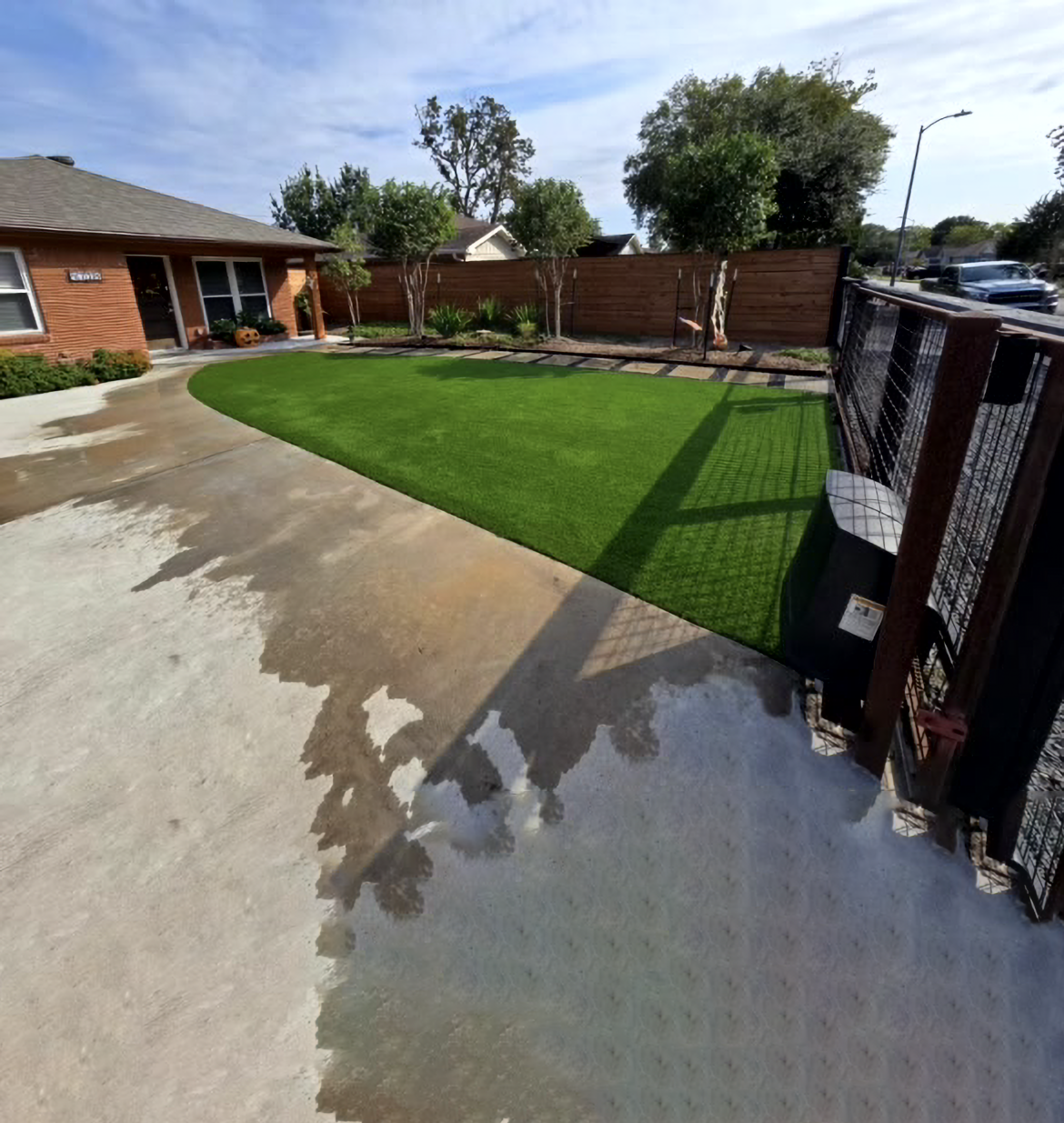 A house with a green lawn, wooden fence, and concrete driveway on a sunny day.