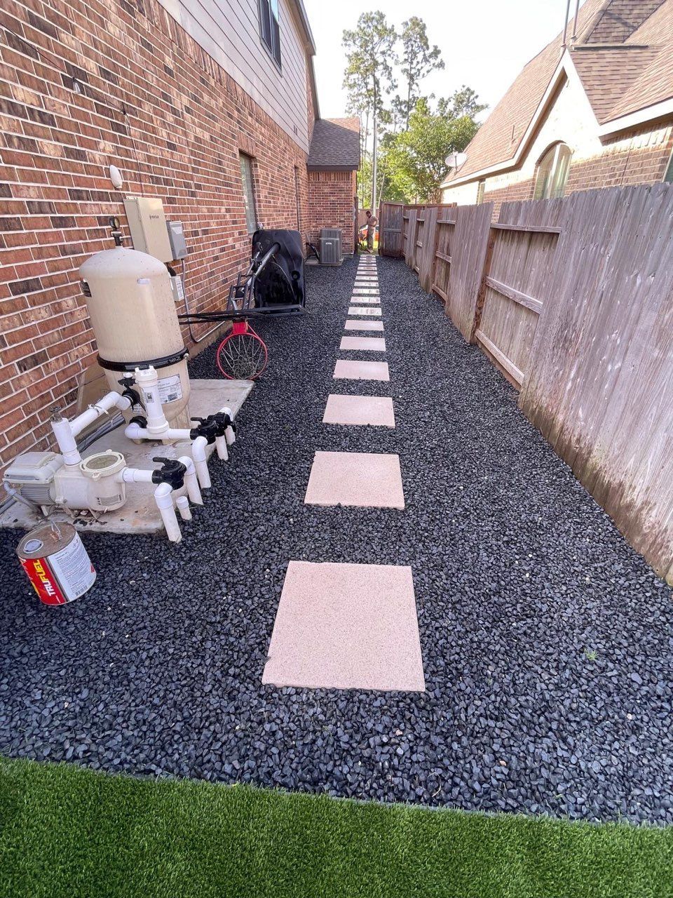 Pathway of stepping stones through black gravel beside a house and fence.