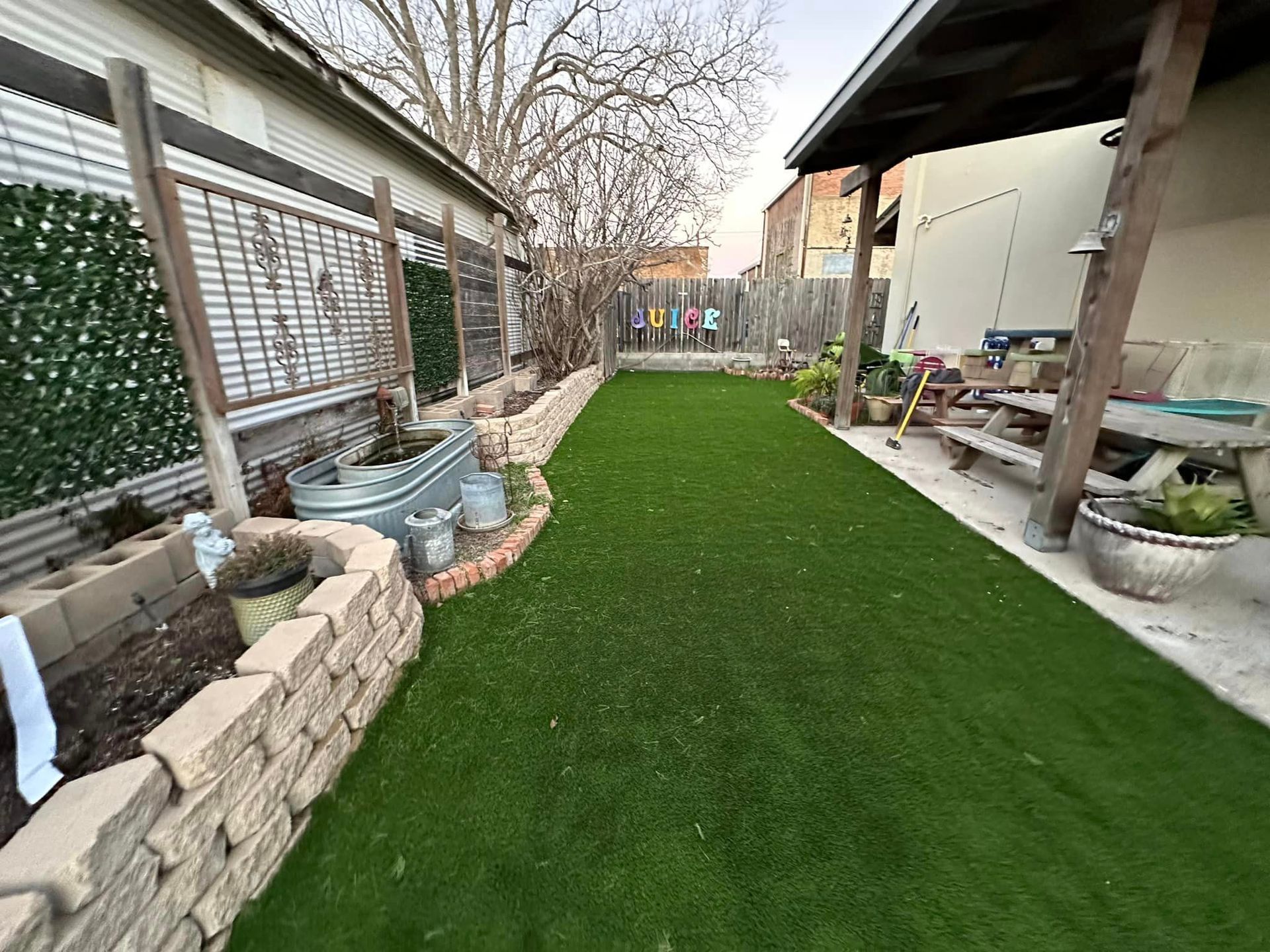 Backyard with green turf, brick borders, and a covered patio area.