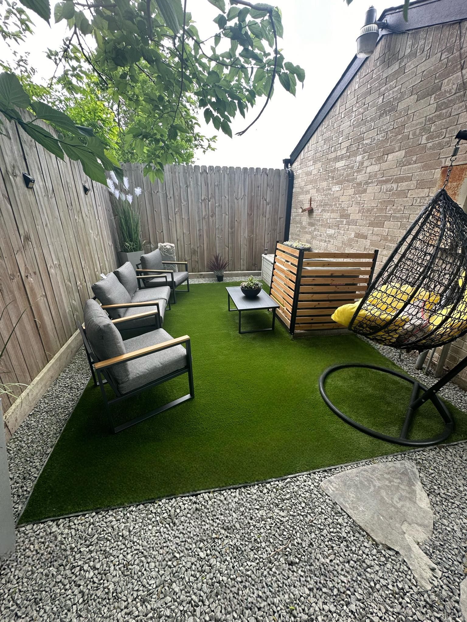 Cozy backyard patio with gray seating, artificial turf, gravel, wooden fence, and hanging chair.