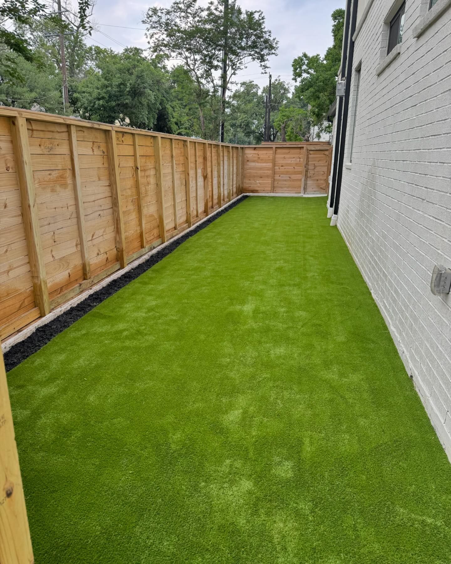 Green artificial turf yard bordered by a wooden fence and a white brick wall.