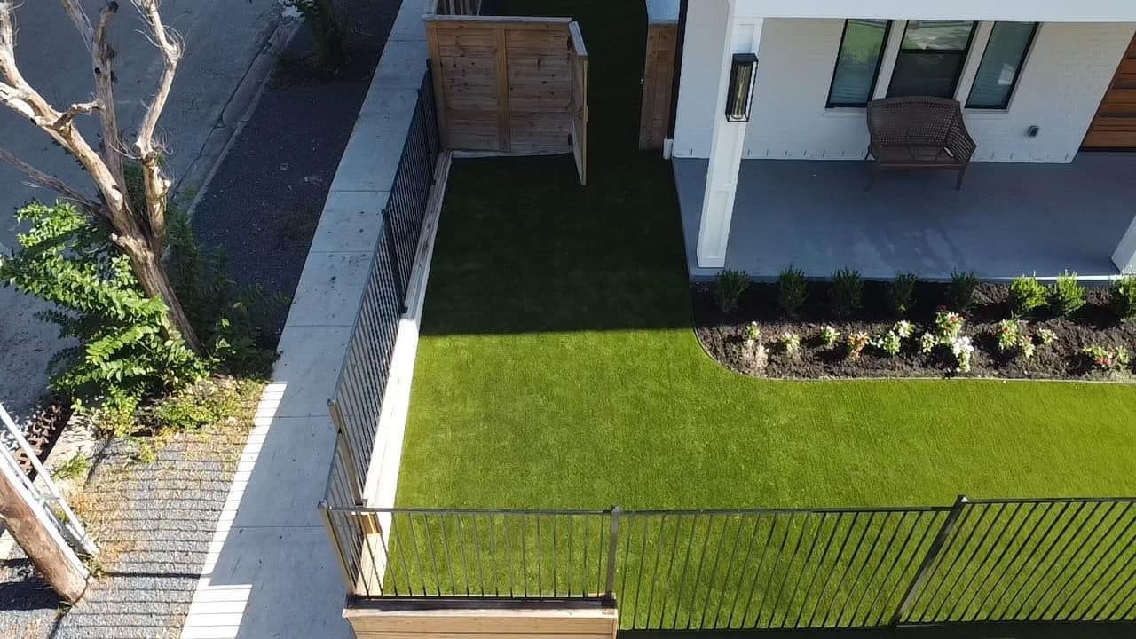 Aerial view of a modern house with a green lawn, fence, and sidewalk.