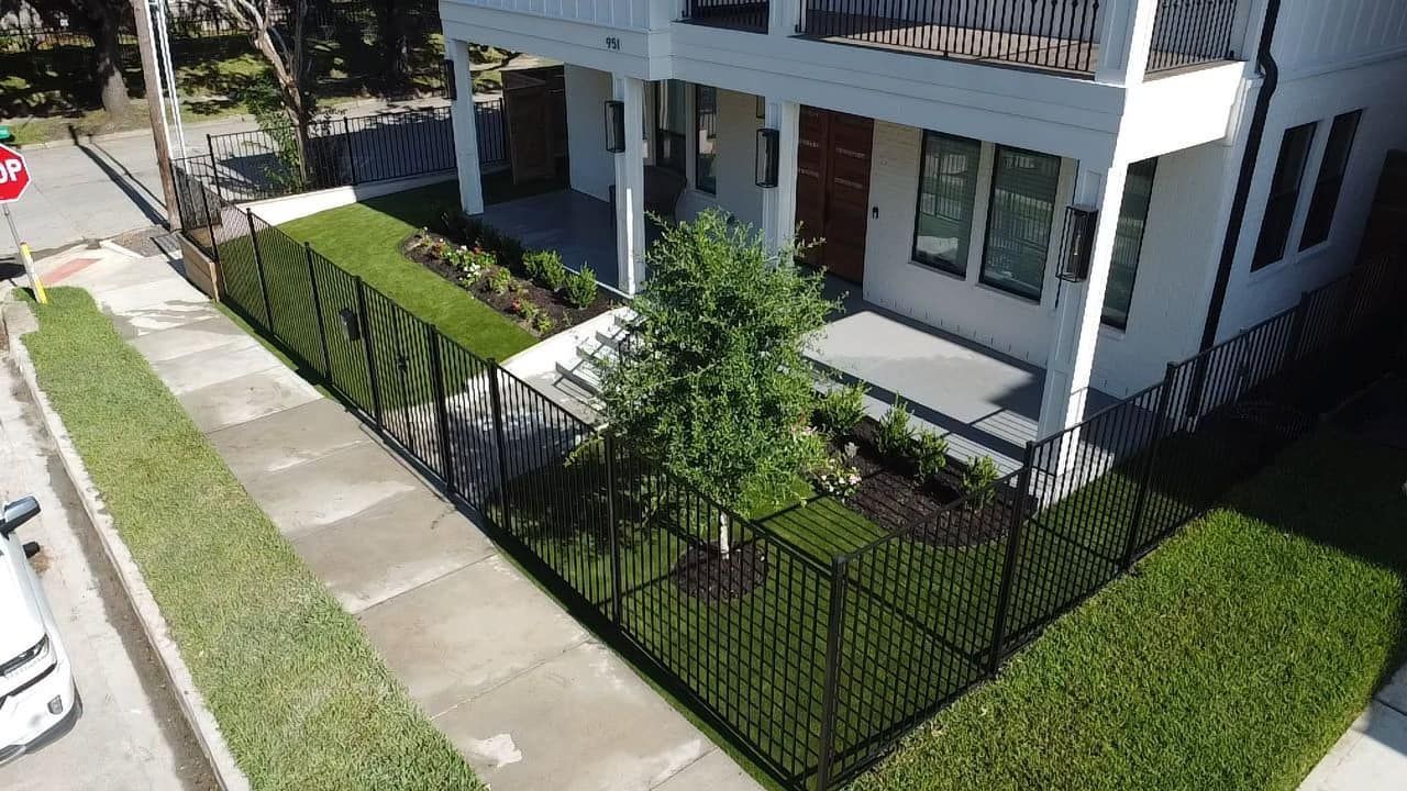 White house with black fence and well-manicured landscaping on a corner lot.