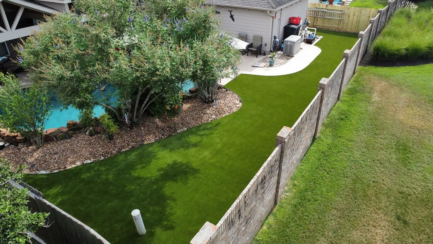 Aerial view of a backyard with artificial turf, a pool, a fence, and a building.