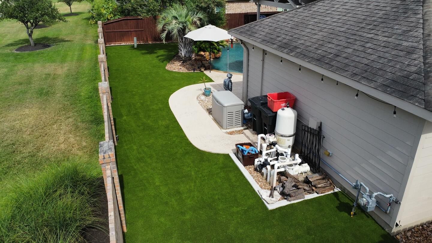 Aerial view of a backyard with green lawn, concrete patio, pool equipment, and a wooden fence.