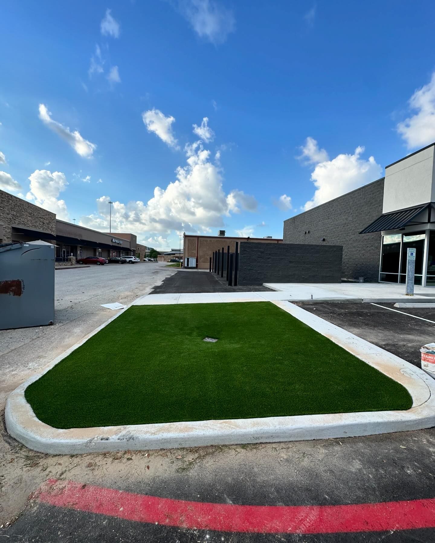 Newly installed artificial grass patch with concrete border, surrounded by asphalt parking area.