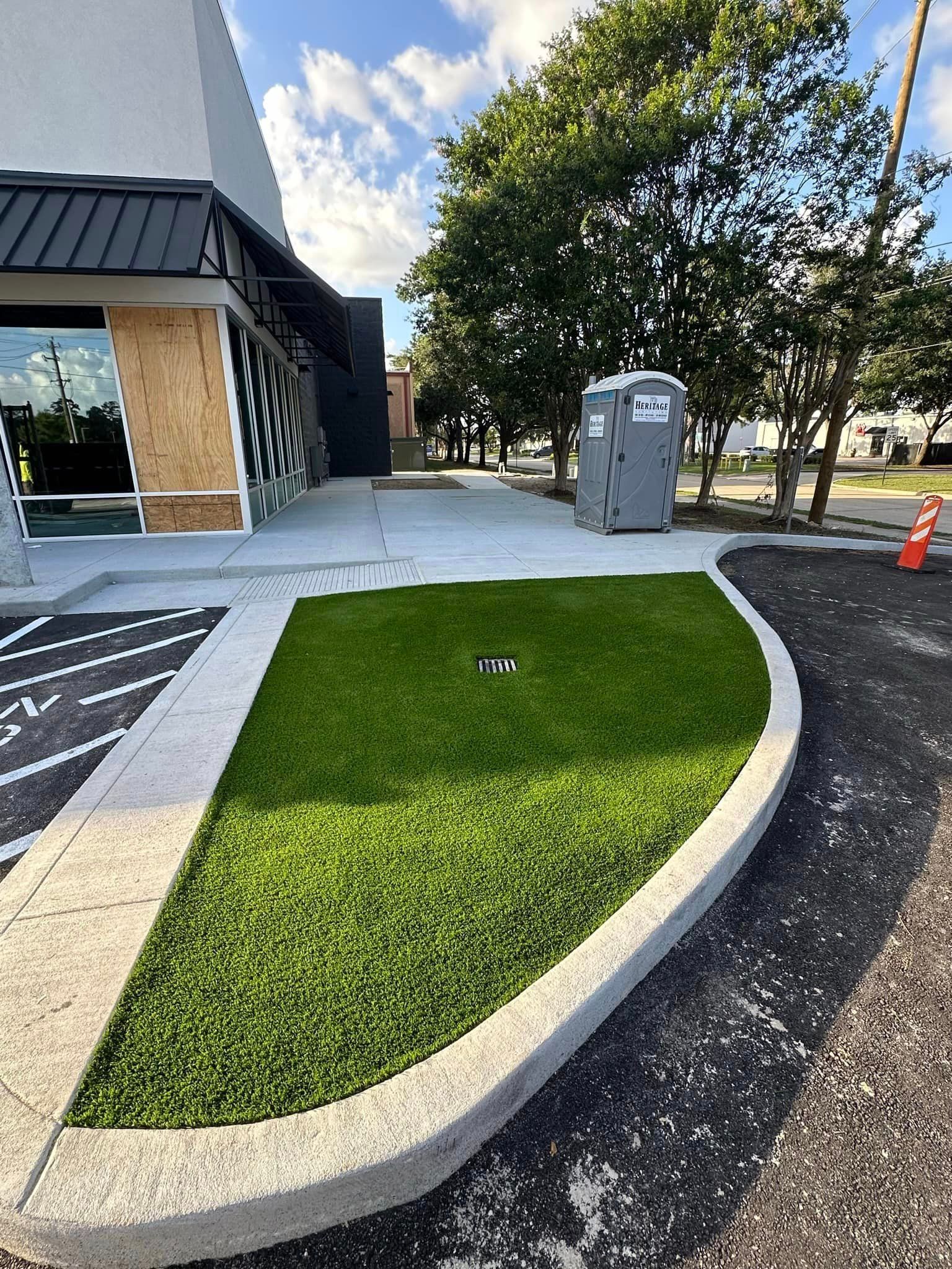 Exterior of building with new lawn and concrete edging; portable toilet and trees in background.