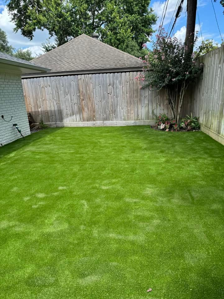Green artificial turf backyard bordered by a wooden fence and a house with a gray roof.