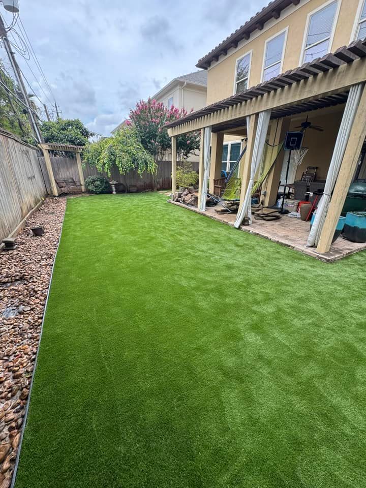 Backyard with green artificial turf, patio, and beige house under a cloudy sky.
