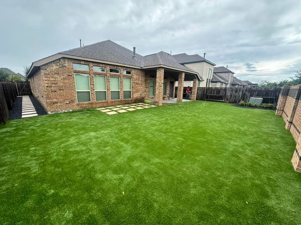 Backyard with brick house, green lawn, paved patio, and wooden fence on an overcast day.