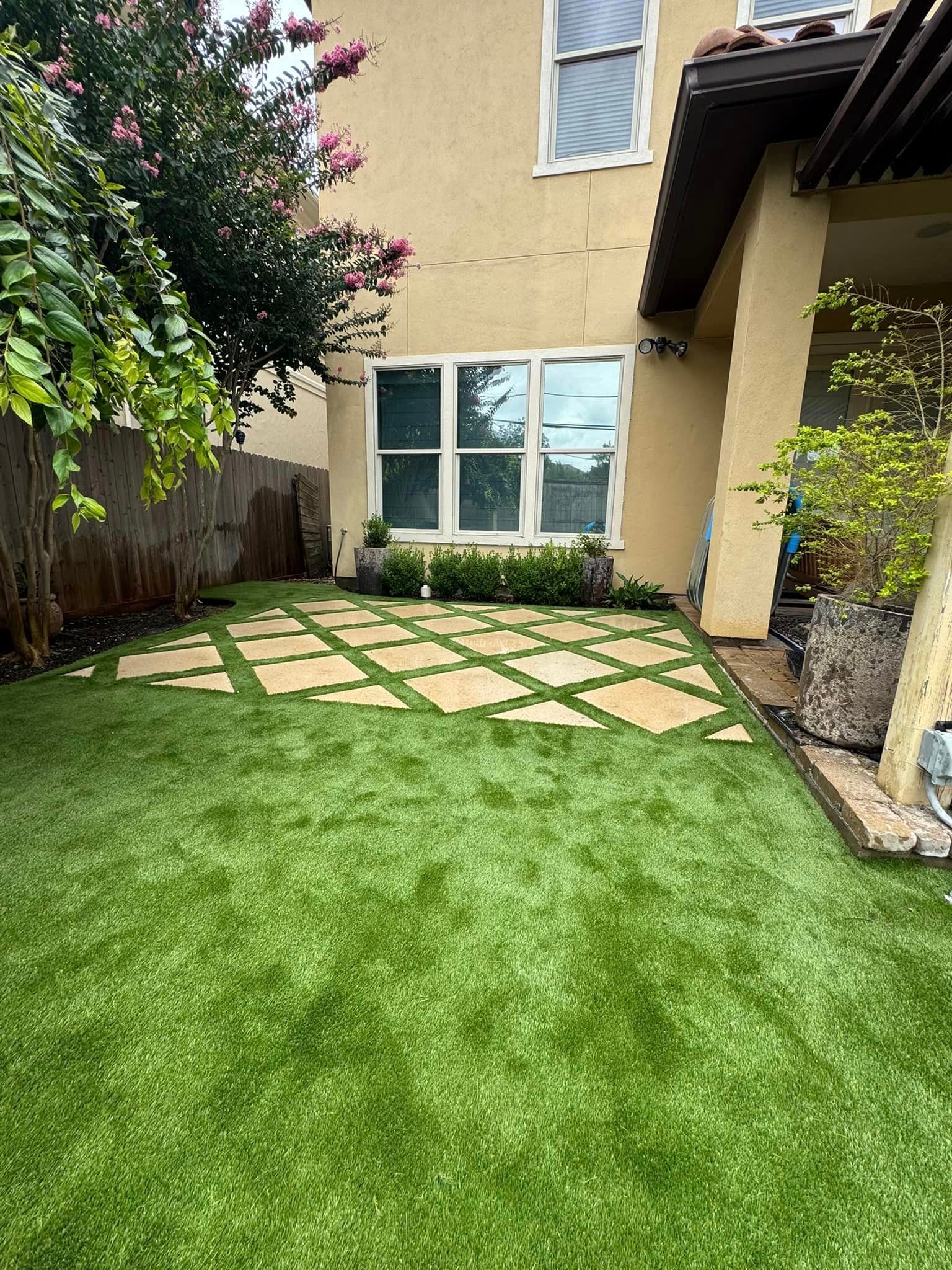 Backyard with artificial turf and stone pathway. Beige house with windows and a covered patio.