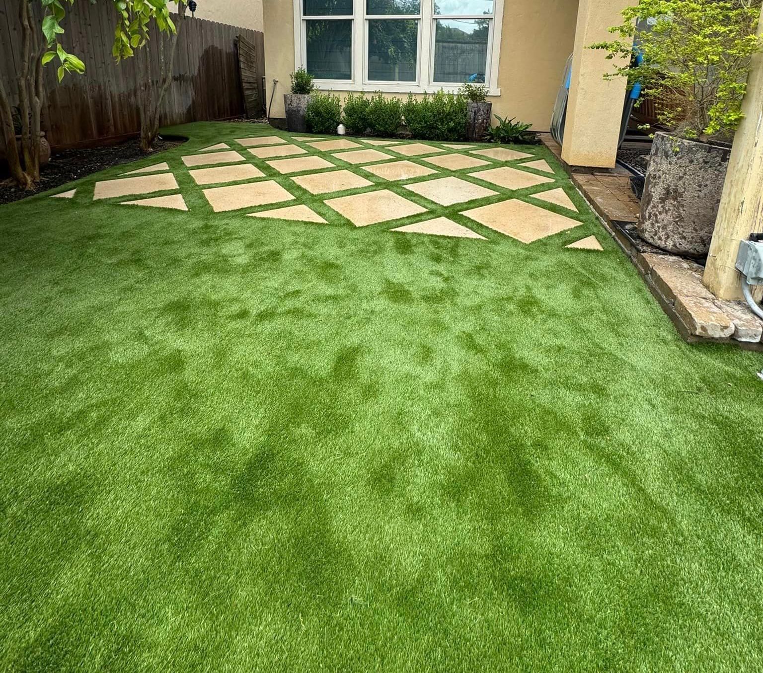 Green artificial turf yard with stone pathway squares leading to a house.