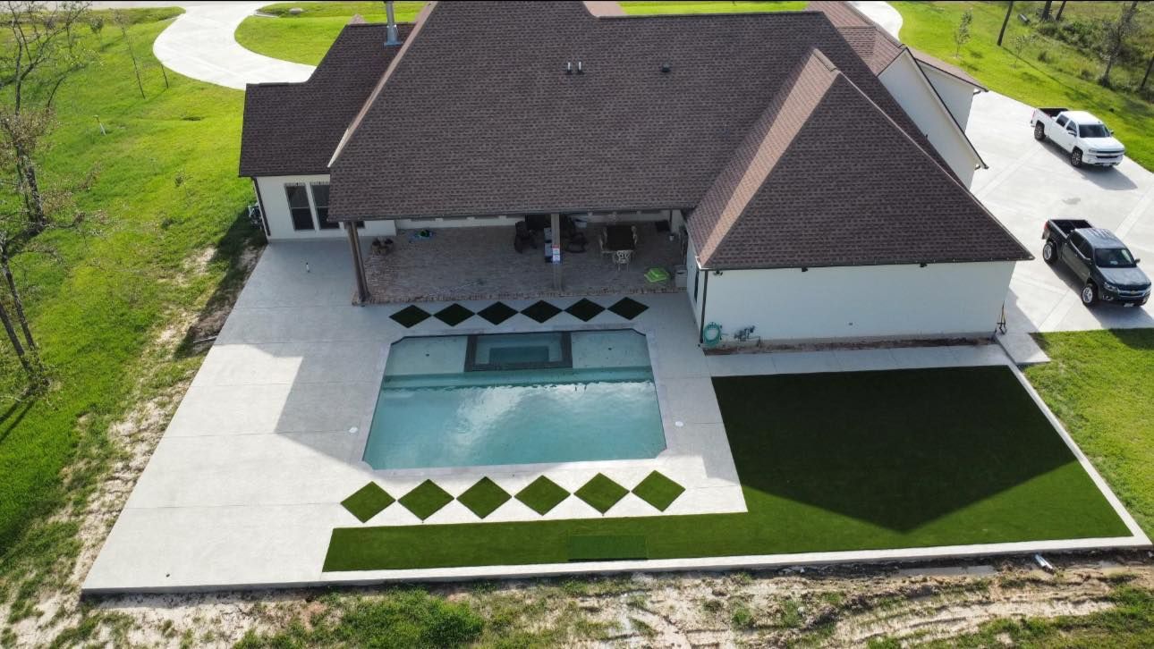 Aerial view of a house with a pool, patio, and green lawn. Two cars are in the driveway.