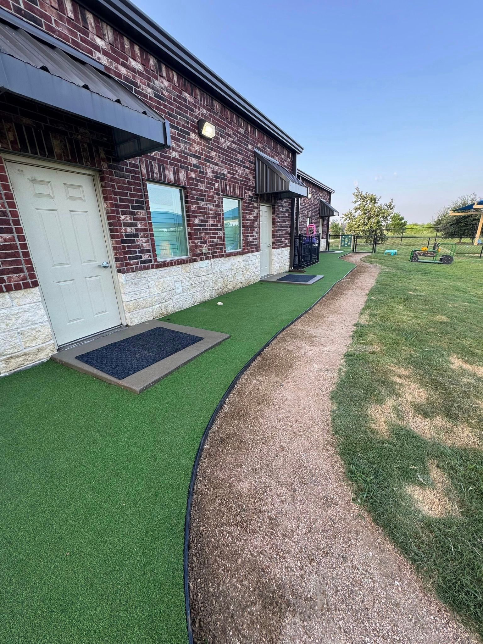 Building exterior with artificial turf lawn, stone path, brick facade, and awning.