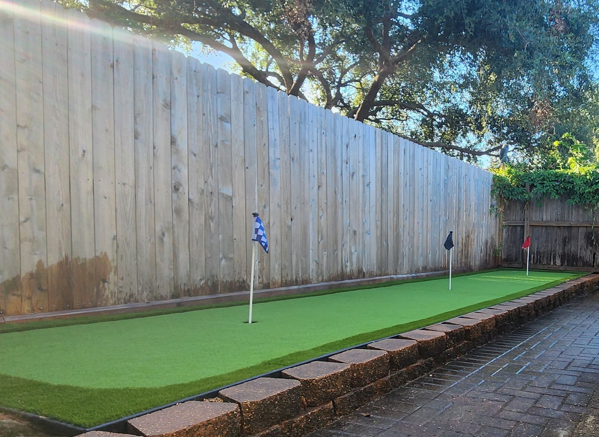 Backyard putting green with three flags against a wooden fence.