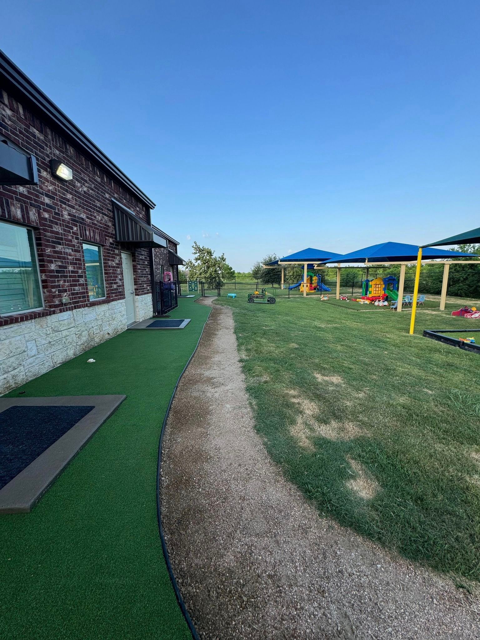 Brick building with a gravel path leading to a playground, under a clear blue sky.