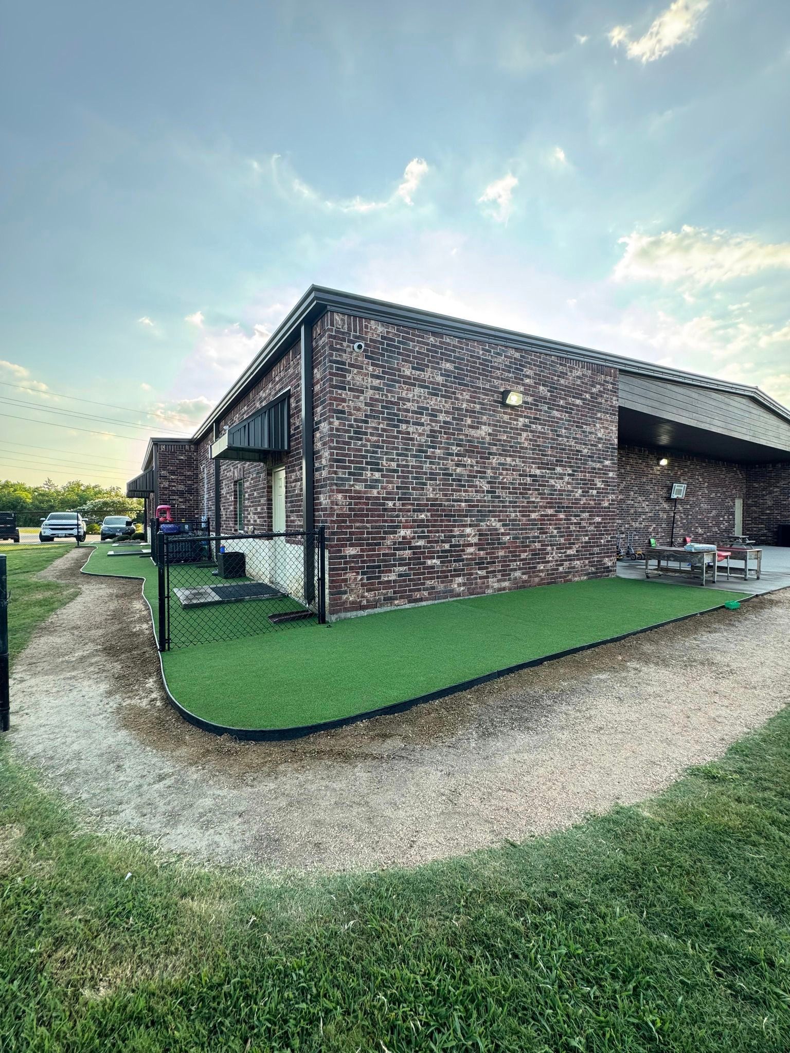 Brick house corner with green trim, gravel path, and grassy yard under a cloudy sky