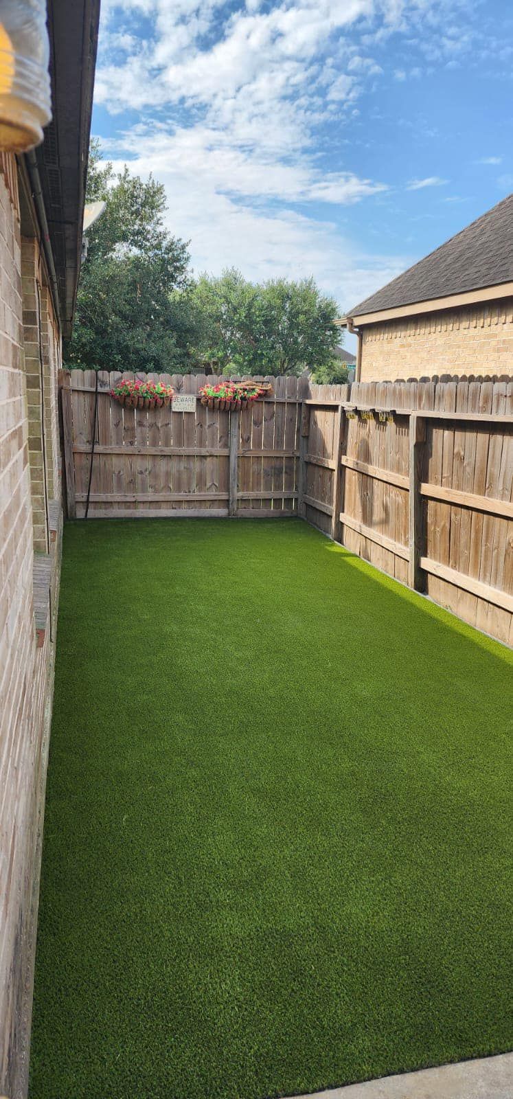Small, fenced backyard with artificial green turf.  Brick wall and wooden fence surround the space, sunny day.