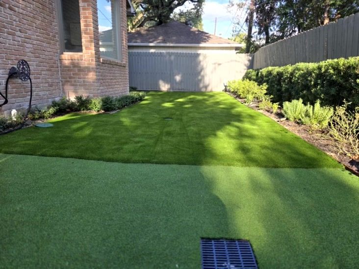 Backyard with green artificial turf, brick wall, and a gray shed.