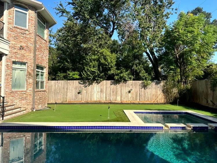 Backyard with brick house, pool, artificial turf, and wooden fence.