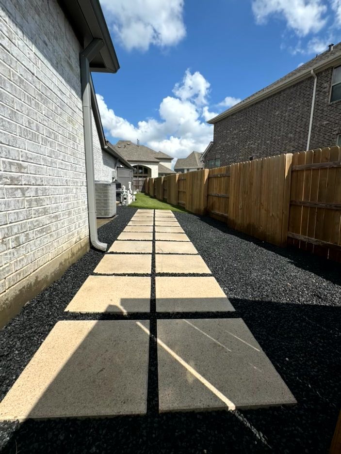 Pathway of concrete stepping stones through black mulch, next to a brick wall and wooden fence.