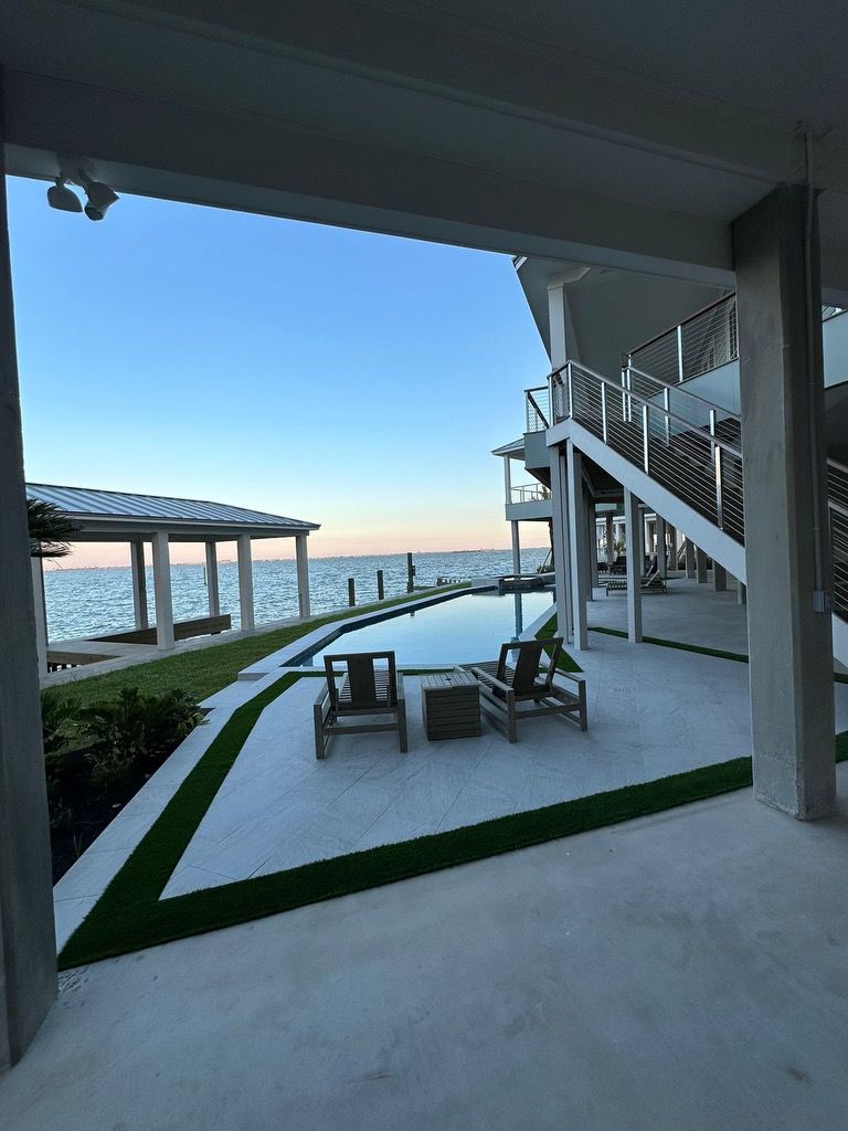 View of a seaside patio with chairs, a pool, and ocean at dusk. Modern architecture.