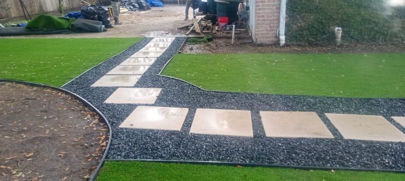 Stone walkway with square pavers and dark rock border on green lawn.