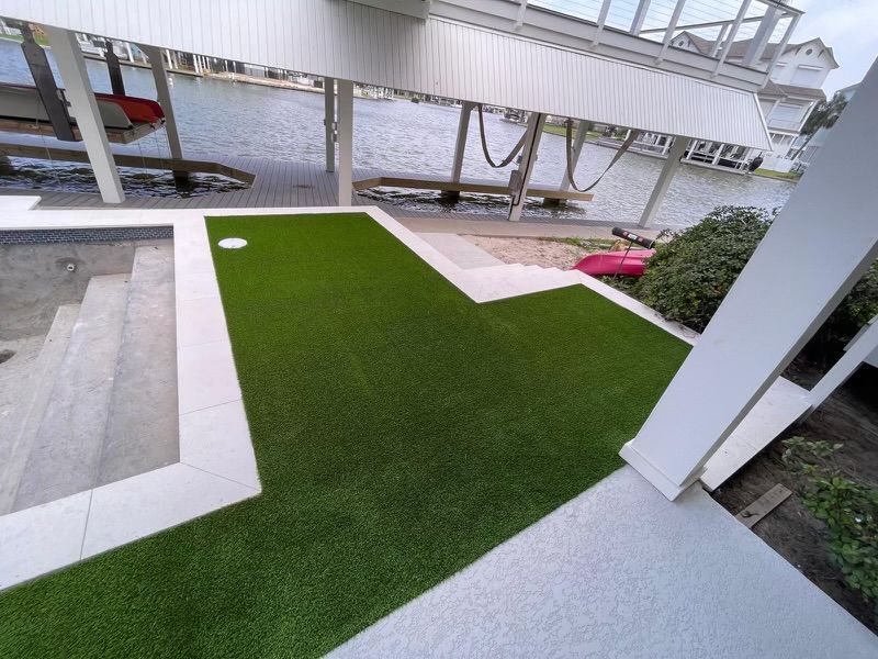 Artificial turf next to a pool and white concrete. A boat lift is visible.