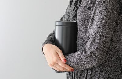 Person in gray sweater holding a black tumbler against a plain background