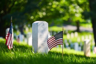 Gravestone with small American flags in a sunny cemetery