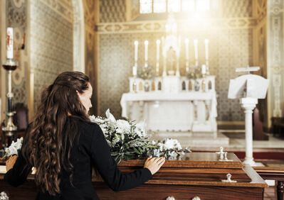 Woman kneeling at a church pew before a white altar with candles and flowers