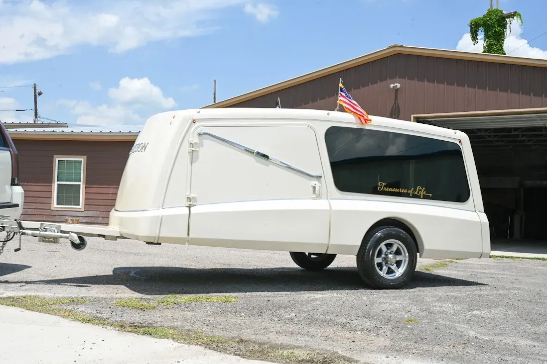White teardrop camper trailer parked on gravel beside a brown building under a blue sky.