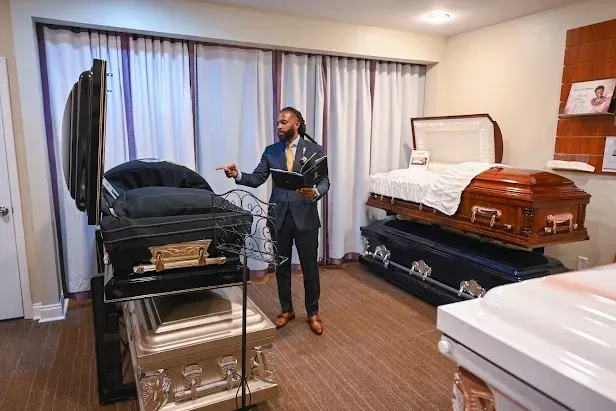 Man standing in a room with several caskets and a covered display table.