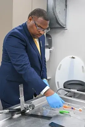 Man in navy suit and gloves working at a lab table with tools and samples in a clinical room