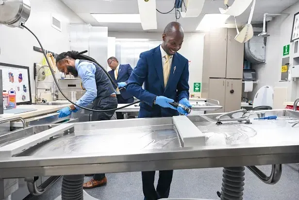 Workers in a bright lab wash a large metal surface with hoses and cleaning tools.