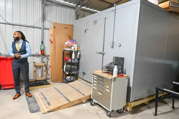 Industrial room with a person standing beside gray storage containers and a metal cabinet on a wooden ramp.