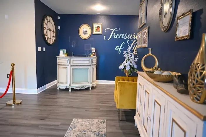 Elegant lobby with blue walls, white console tables, gold decor, and “Treasures” wall sign