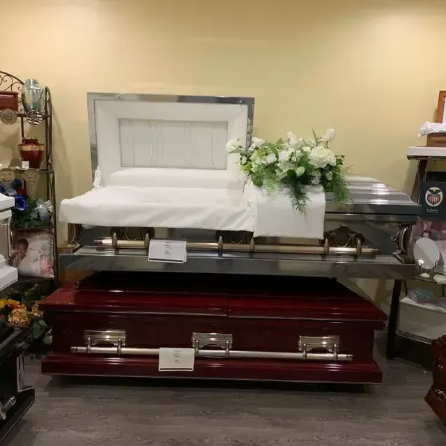 White casket with flowers displayed on a red casket stand in a funeral home showroom