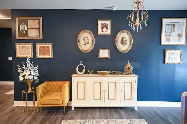Elegant room with navy accent wall, framed art, cream sideboard, mustard chair, and chandelier