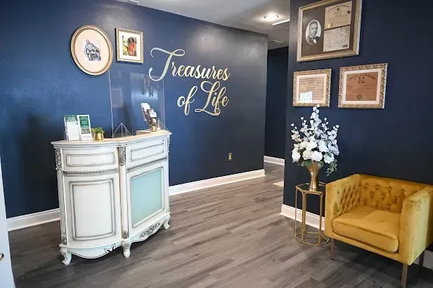 Elegant reception area with navy walls, white desk, gold chairs, and “Treasures of Life” sign