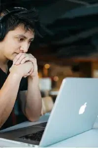 Person thinking while using a laptop in a dimly lit room