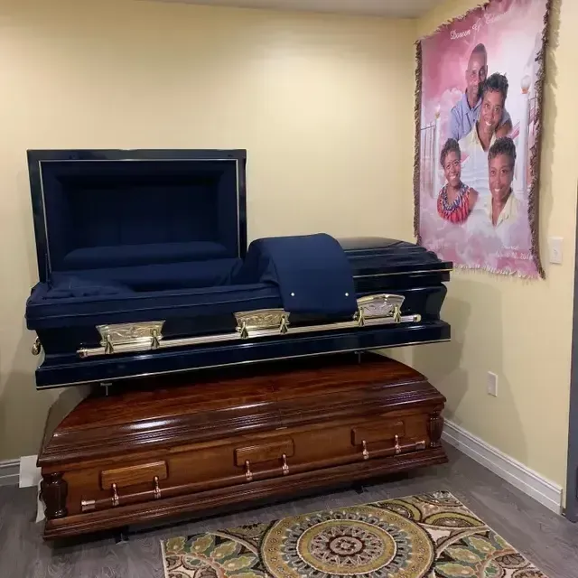 Two open caskets in a room, one dark blue and one wooden, with a memorial photo on the wall.