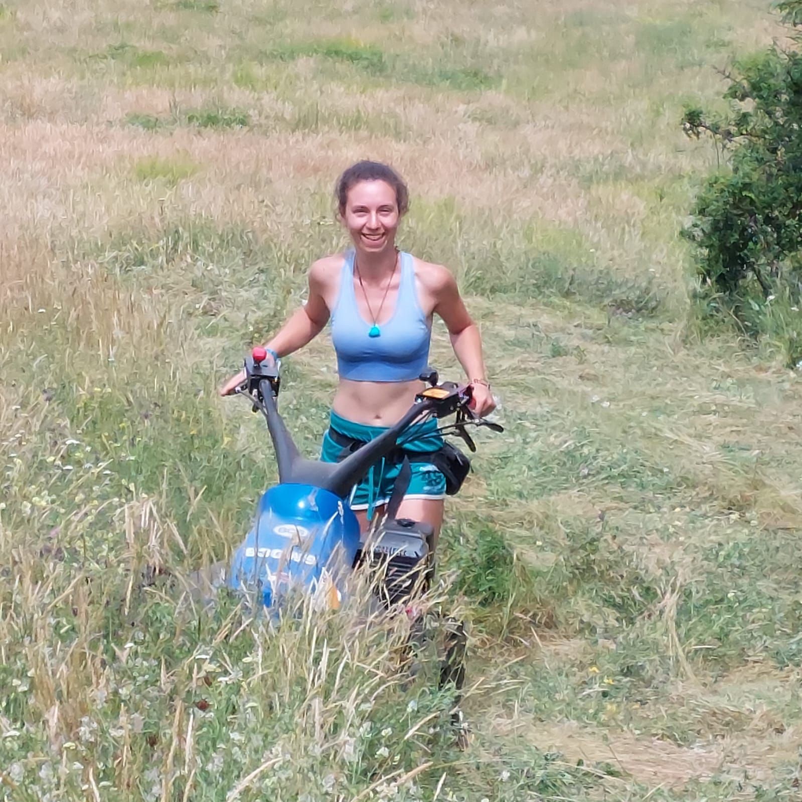 Una persona spinge un tosaerba blu attraverso l'erba alta in un campo.