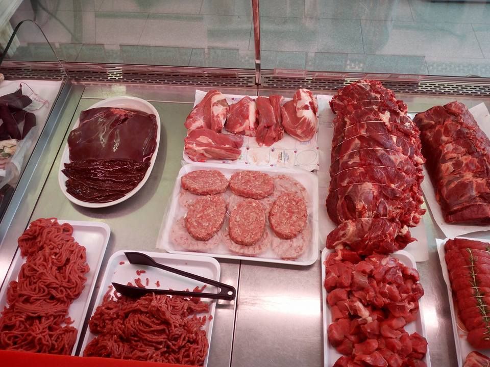 Banco macelleria con assortimento di carni crude, salsicce e bistecche esposte su vassoi e su una superficie metallica.