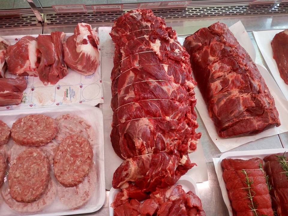 Assortimento di carni crude e salsicce esposte su vassoi al banco di una macelleria.