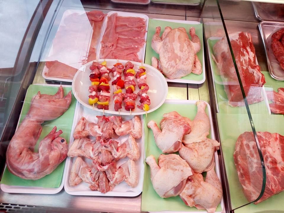 Assortimento di carni e pesce crudi esposti in una vetrina refrigerata, con vassoi di pollo, pesce e condimenti a cubetti.