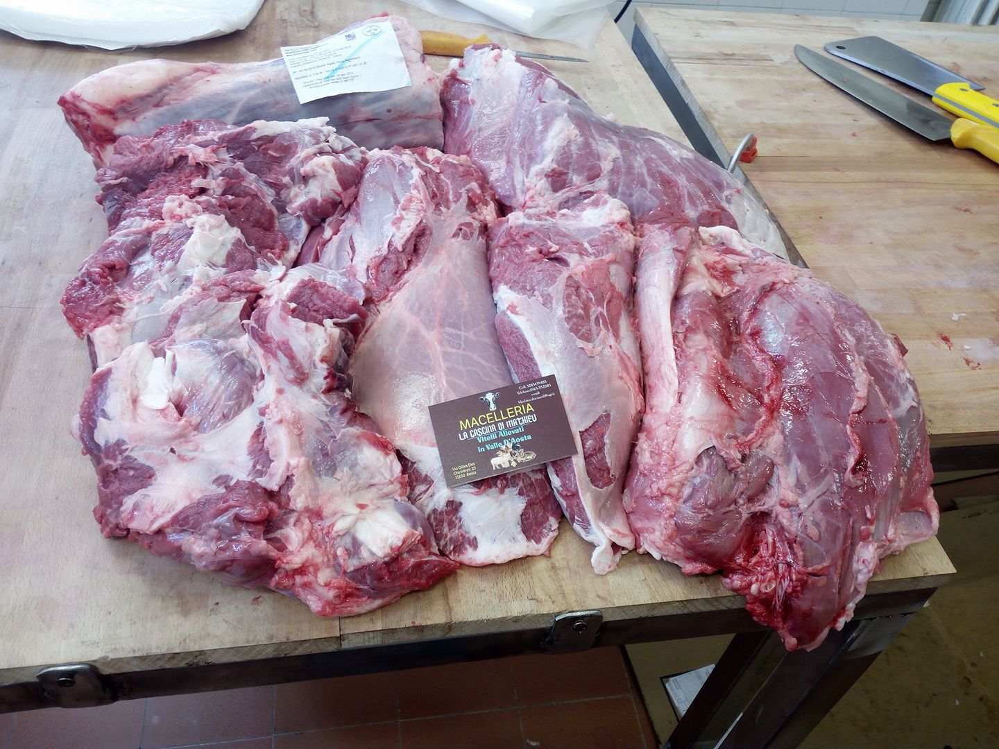 Tagli di carne cruda su un tavolo di legno con coltelli nelle vicinanze, in una cucina o in una zona di preparazione.